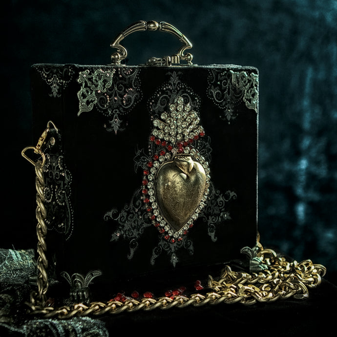 Sagrado corazón dorado rodeado de cristales sobre cartera en terciopelo negro y dorado