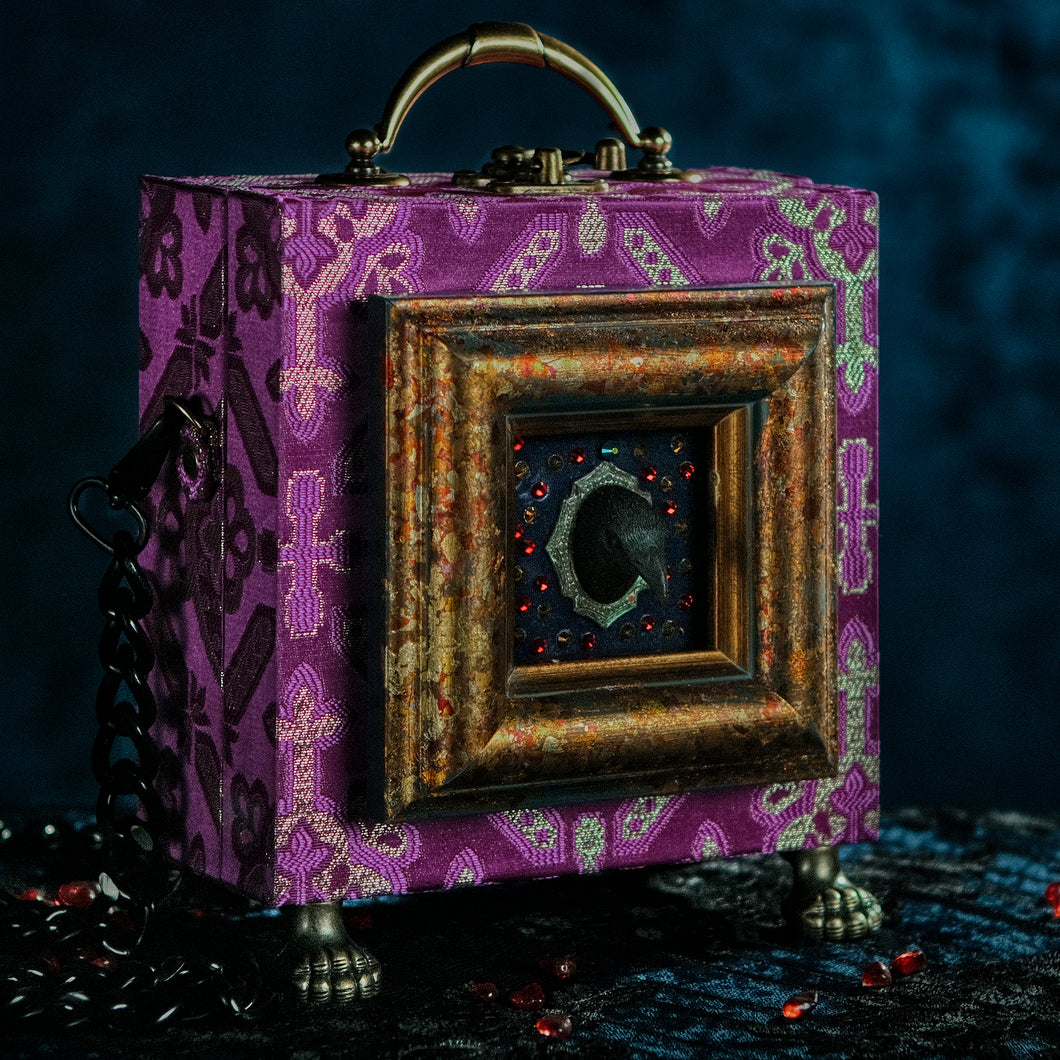 Framed raven head on purple and silver brocade hand bag
